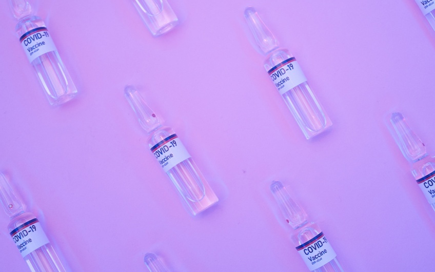 COVID vaccine vials arranged in a pattern on top of fuschia paper