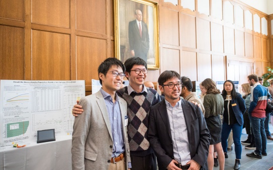 Three Ford School graduate students in the Great Hall, beneath a portrait of President Ford