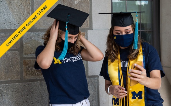 Photo of two Ford School graduates wearing their mortar board caps, stole, and Ford School t-shirts. A text banner angled at 45 degrees in the upper left corner reads "Limited-time online store"