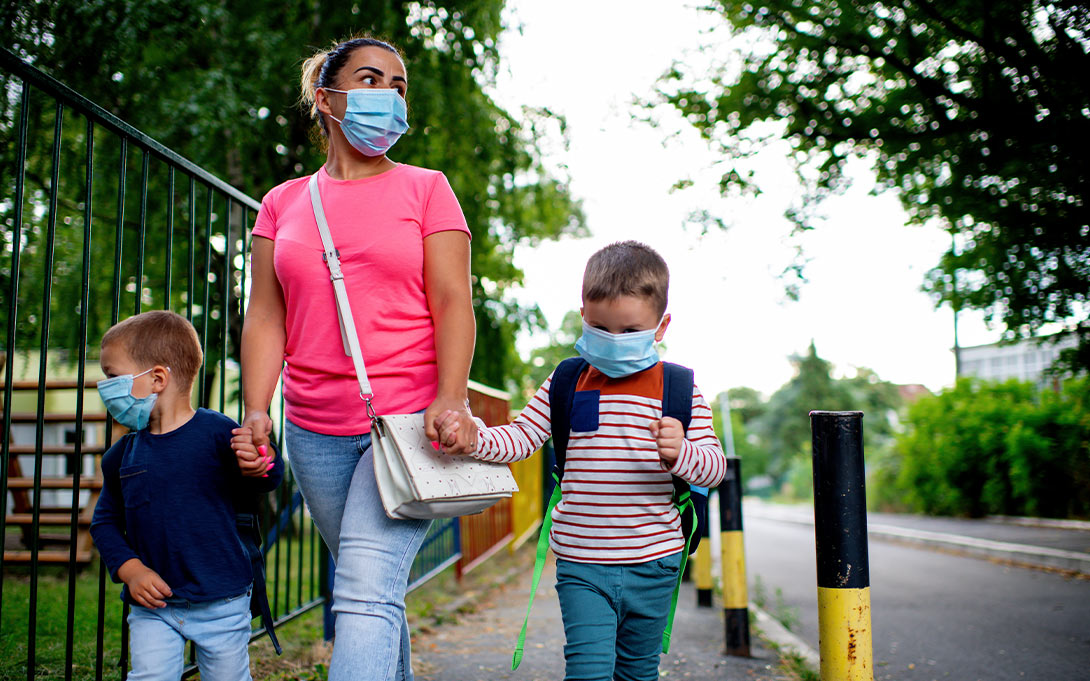 A parent/guardian and two young children in masks walking outdoors (Credit: Shutterstock)