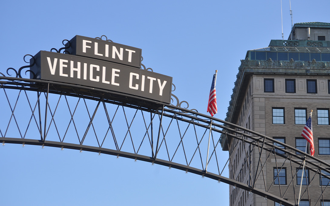 Photo of a large metal arch with a sign reading "Flint: Vehicle city" at a gateway to Flint, Michigan