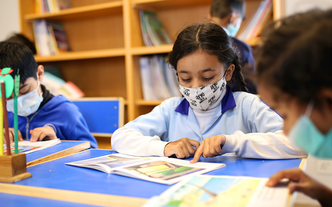 Photo of young students, each reading a book, seated around a small classroom table