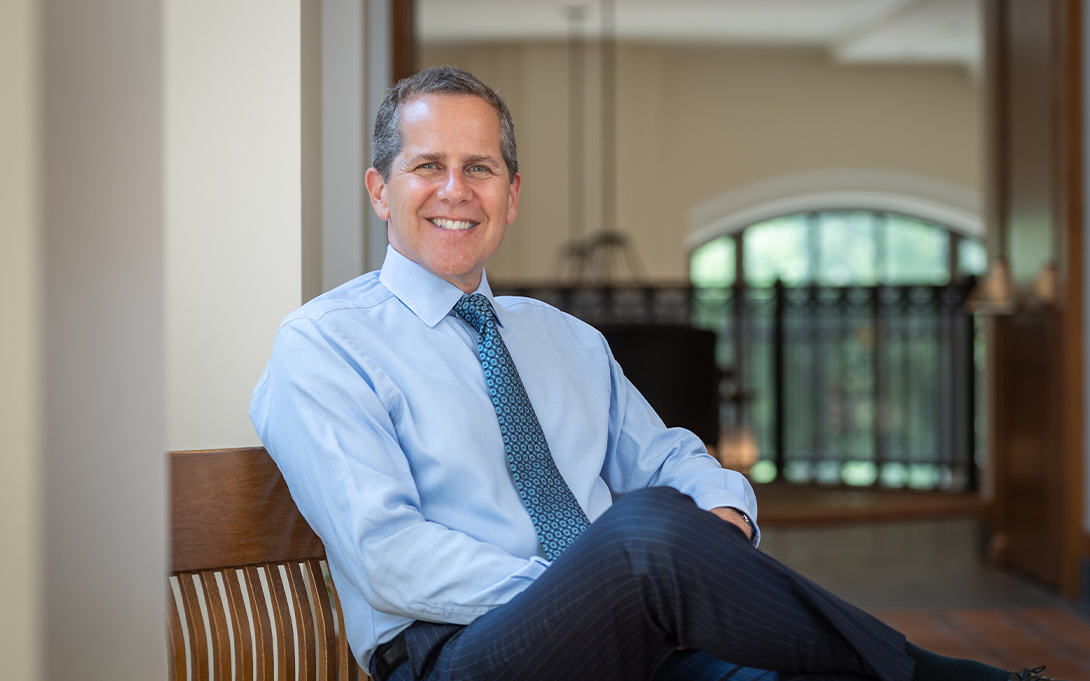 Photo of Michael S. Barr in 2020, seated on a bench in Weill Hall's second floor hallway