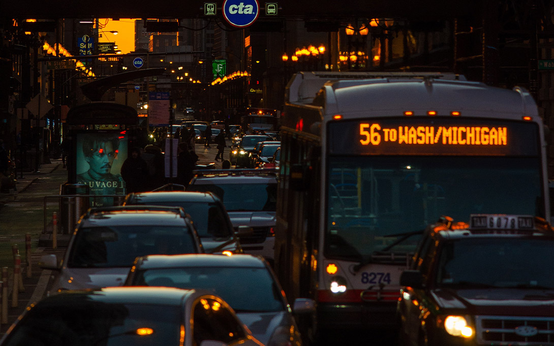 Photo of cars and buses driving on a Chicago street as the Metro train passes overhead on an elevated platform