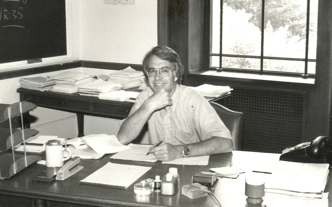 Photo of Ned Gramlich seated at his desk on campus