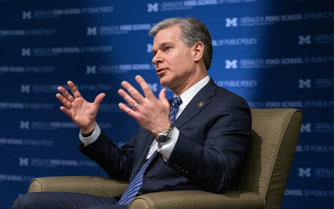 Photo of FBI Director Christopher Wray, seated in front of a blue Ford School backdrop, responding to a question