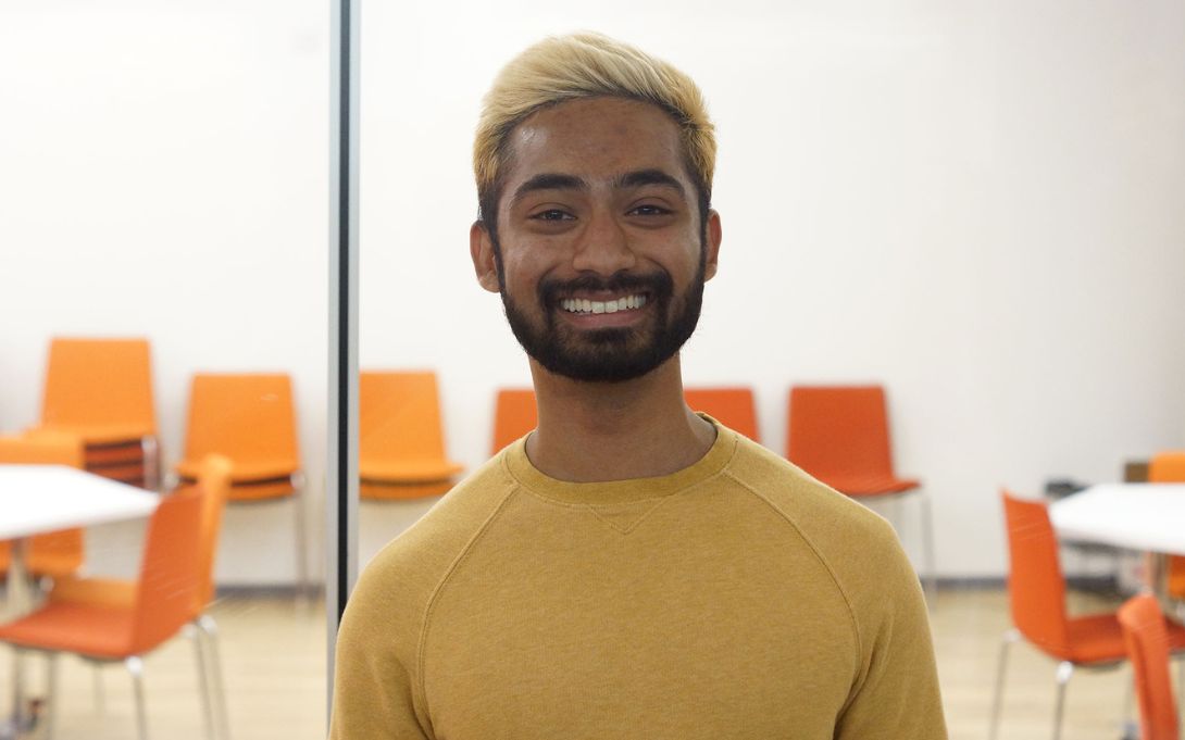 Alvin Christian smiling in an office space with tables and orange chairs in the background