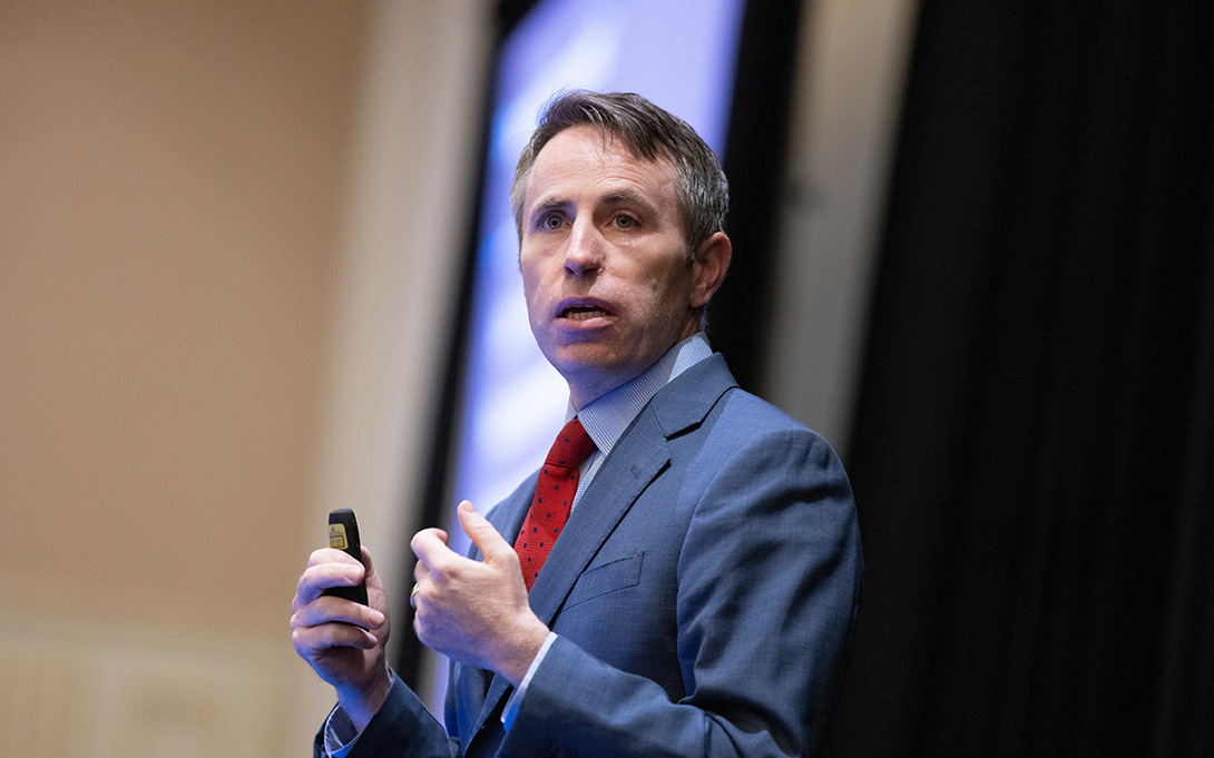 Person giving a presentation with a remote in hand, standing in front of a screen displaying a presentation slide.