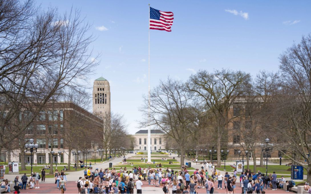 university of michigan diag with the american flag waving in the center, students bustle around campus