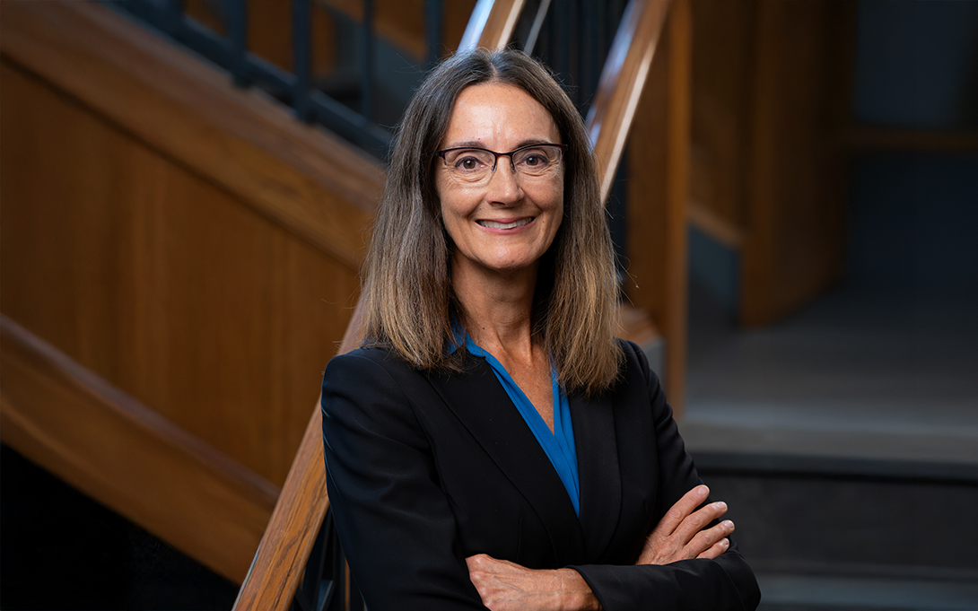 Portrait of a smiling person wearing a business suit, standing in front of wooden stair railings.