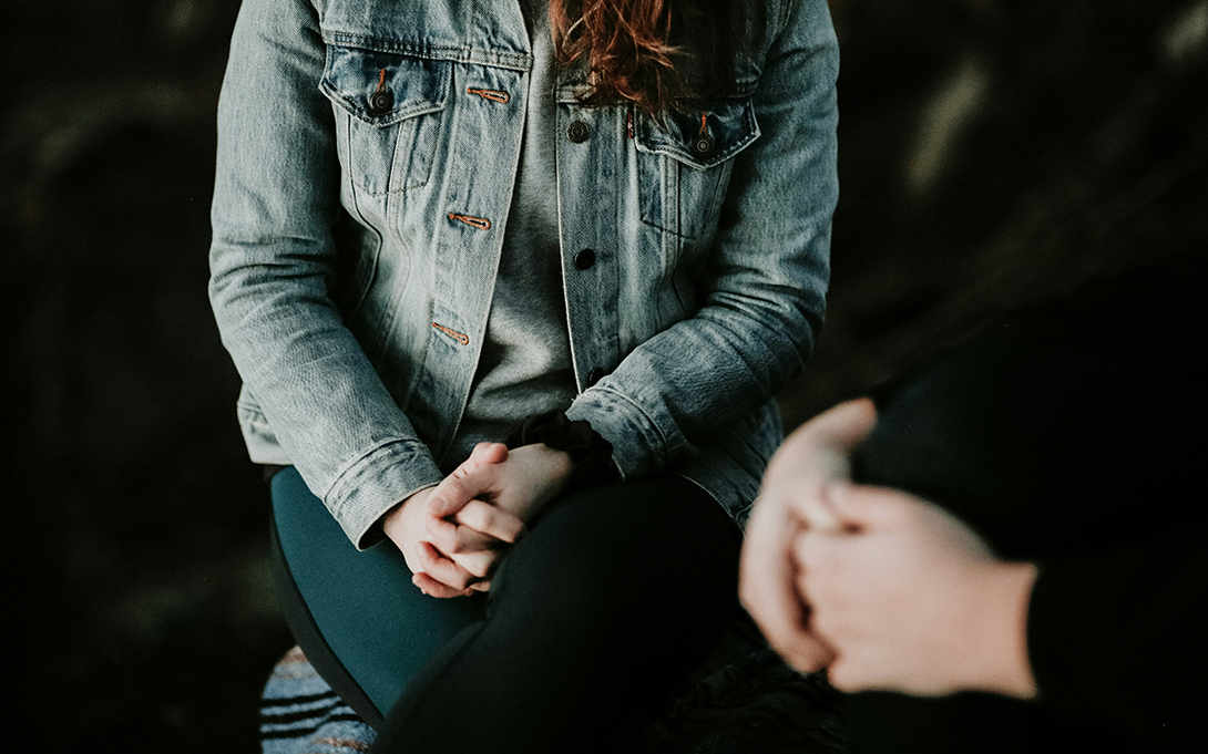 The cover photo of the project aware grant report: the image of the middle part of the body of two people sitting close to each other during a conversation.