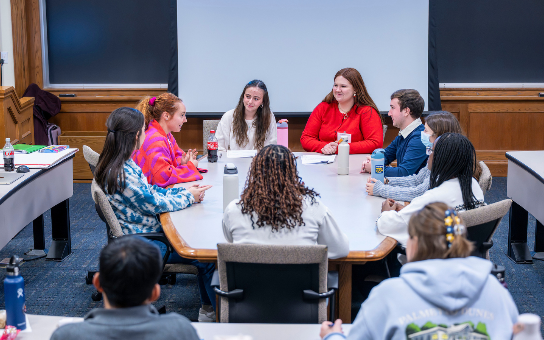 Group of students sitting around a table in a classroom engaging in a discussion.