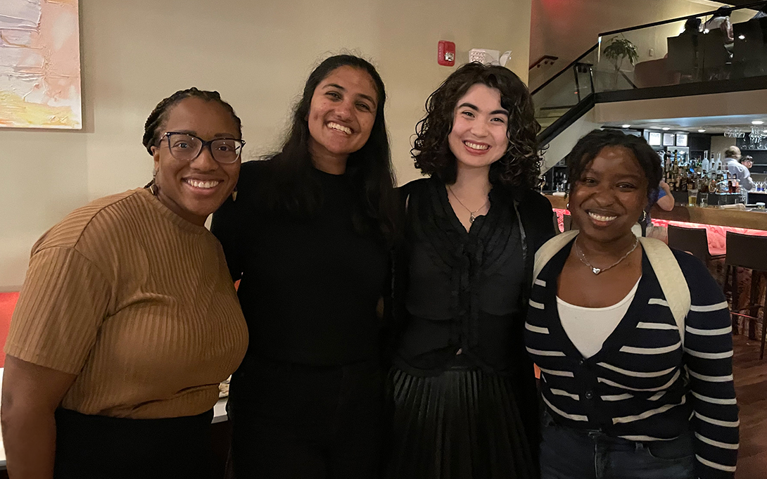 Four people smiling and posing together inside a restaurant