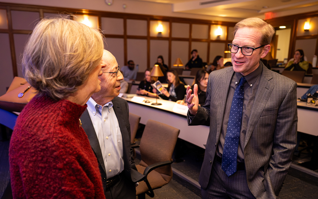 A person having an animated conversation with two other people in a university classroom