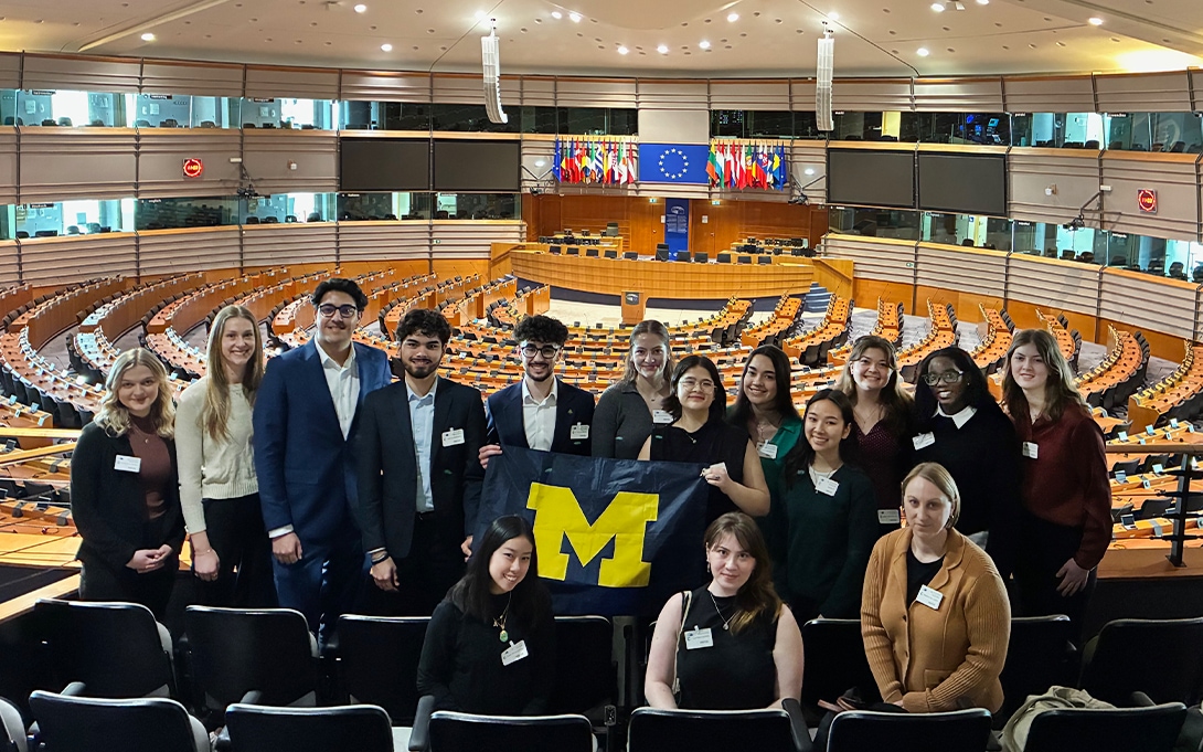 A group of undergraduate students holding a Ford School flag at the European Parliament