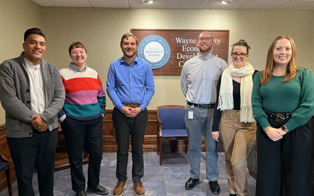 Six people stand together in front of a Wayne County Economic Development Corporation sign during a visit with Ford School Consulting Clinic students.