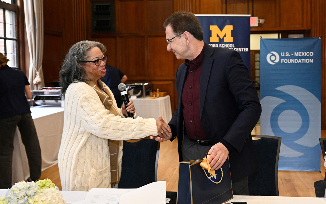 Two people at an event holding gift bags and shaking hands