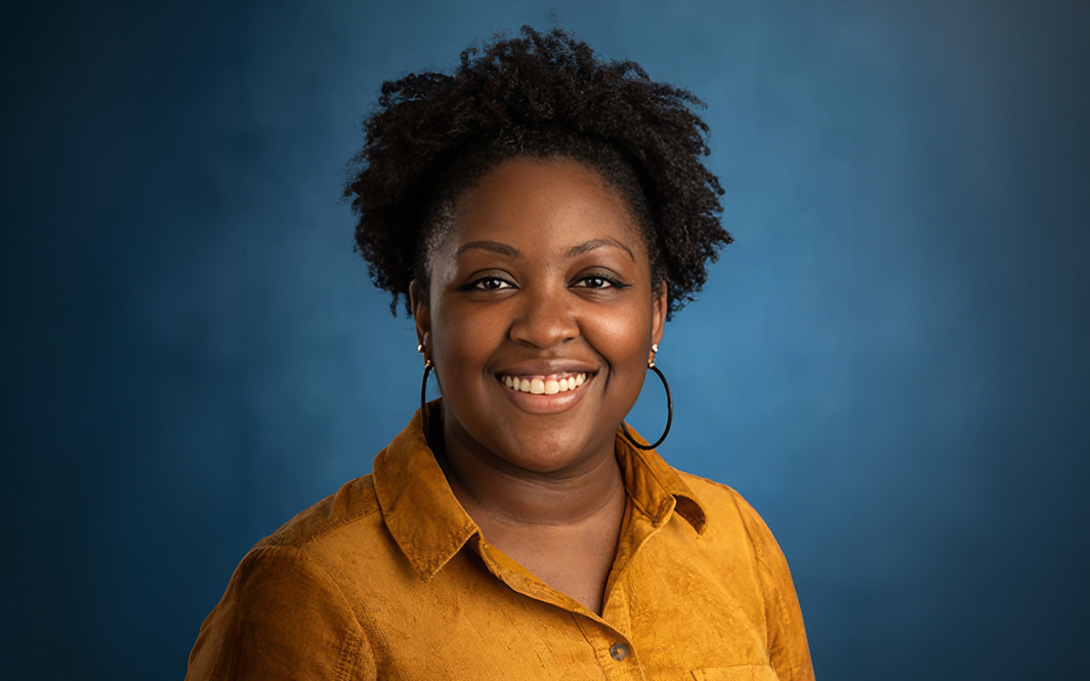 A headshot of a smiling person in a yellow shirt against a blue background