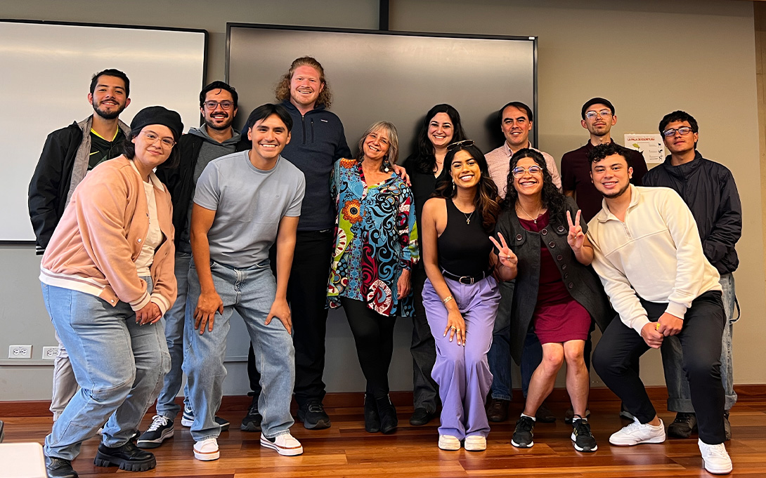 A group of people poses for a photo in a classroom, standing in front of a whiteboard.