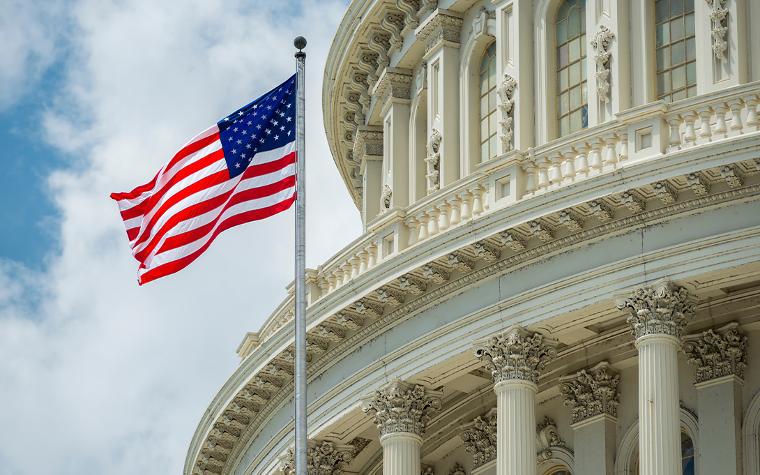 An American flag billowing in the wind beside a government building.