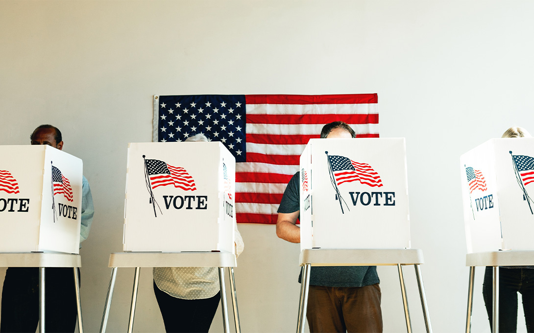 Voters standing in their voting booths with an American flag behind them.