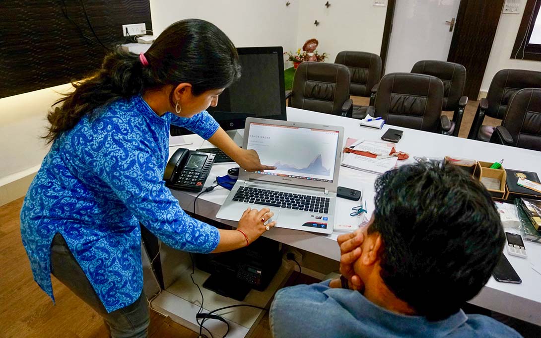A woman presents the work on her computer screen to a colleague who sits nearby.