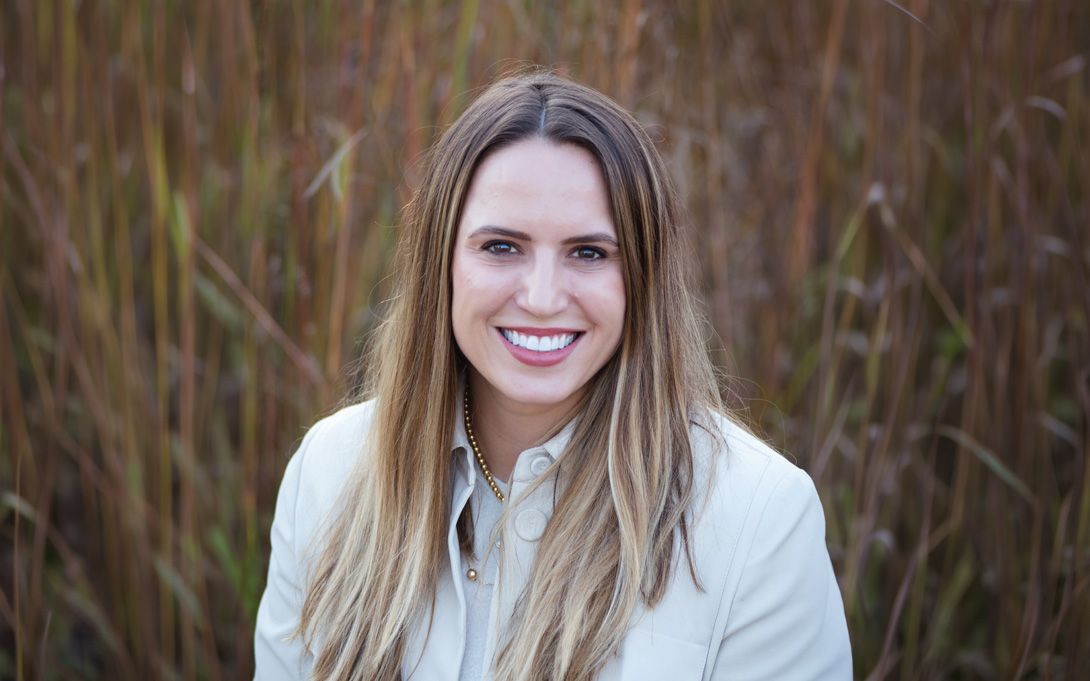 A person smiling shown against a blurry nature background.