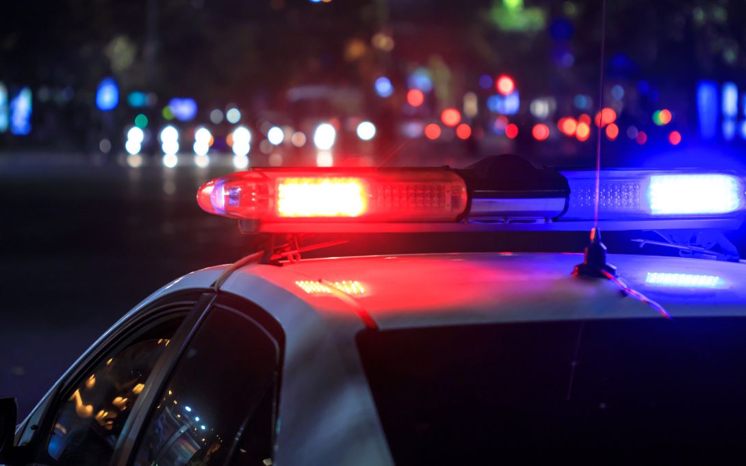 Close-up of flashing red and blue lights atop a police car at night, with blurred traffic in the background.