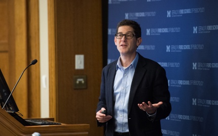 Photo of Brian Jacob standing at the Annenberg Auditorium podium, delivering remarks at a public event