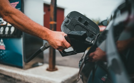 Photo of a person's arm holding a gasoline pump nozzle in position as it dispenses fuel into a black vehicle