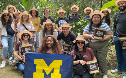 Smiling students in straw hats in Colombia holding a University of Michigan Block-M flag