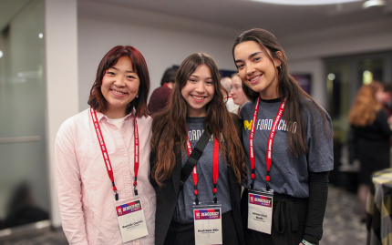 Three individuals wearing lanyards smiling at a conference event.