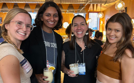 Four individuals posing with beverages at a social gathering.