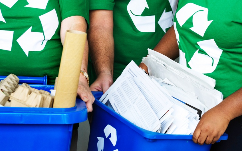 People wearing shirts with the recycling logo and holding recycling bins full of recyclable items