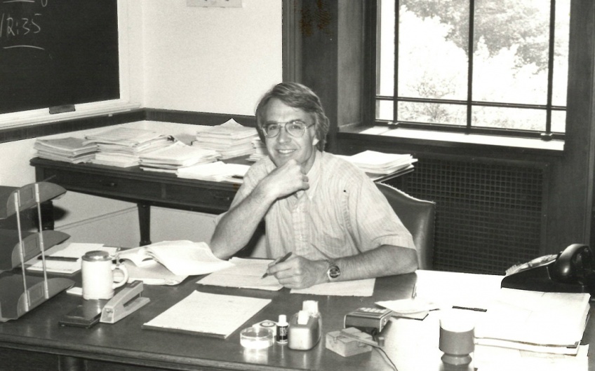 Photo of Ned Gramlich seated at his desk on campus