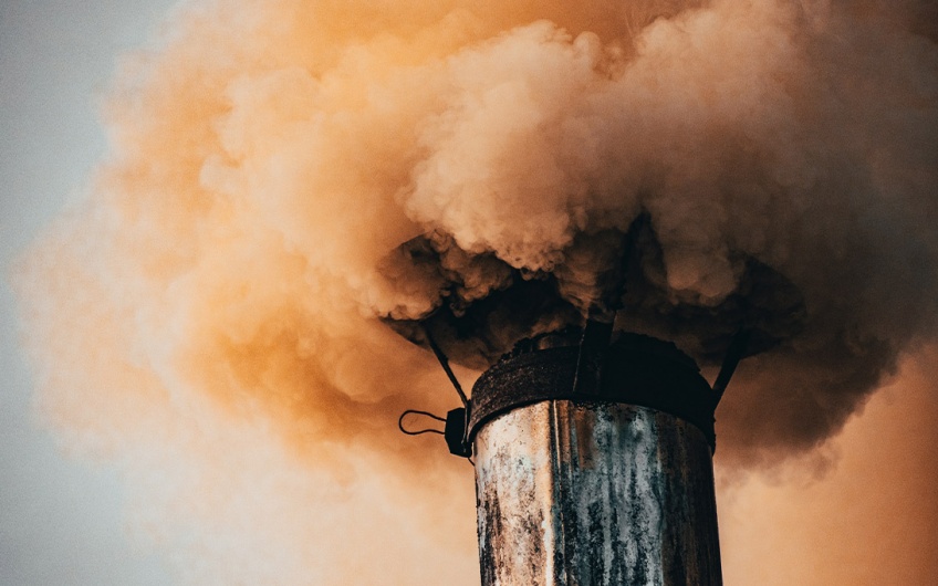Photo of smoke billowing out of an old rusting gray exhaust vent atop a tower