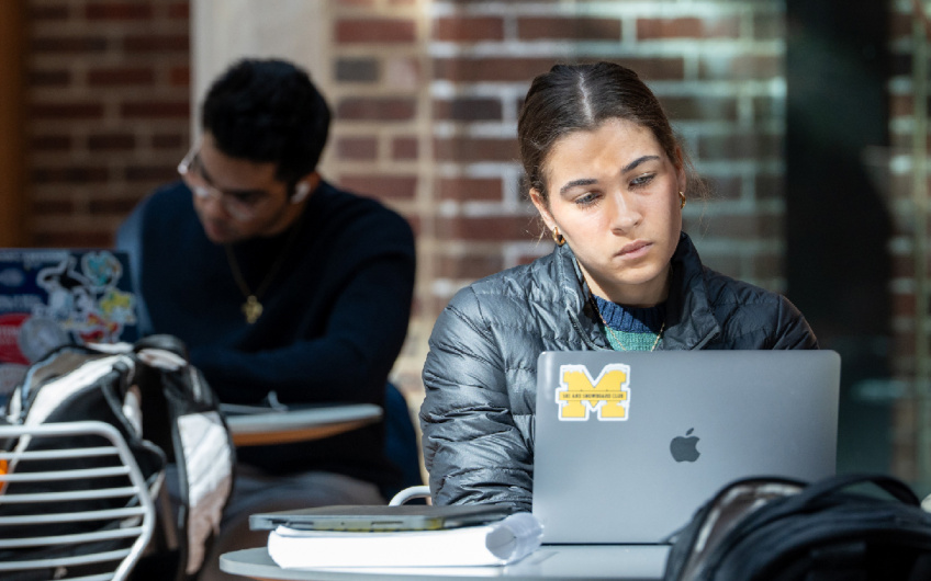 Image of two students working at their laptops in a brick building