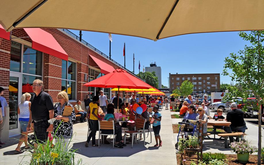 People sharing a public space with greenery, tables, umbrellas, and open space