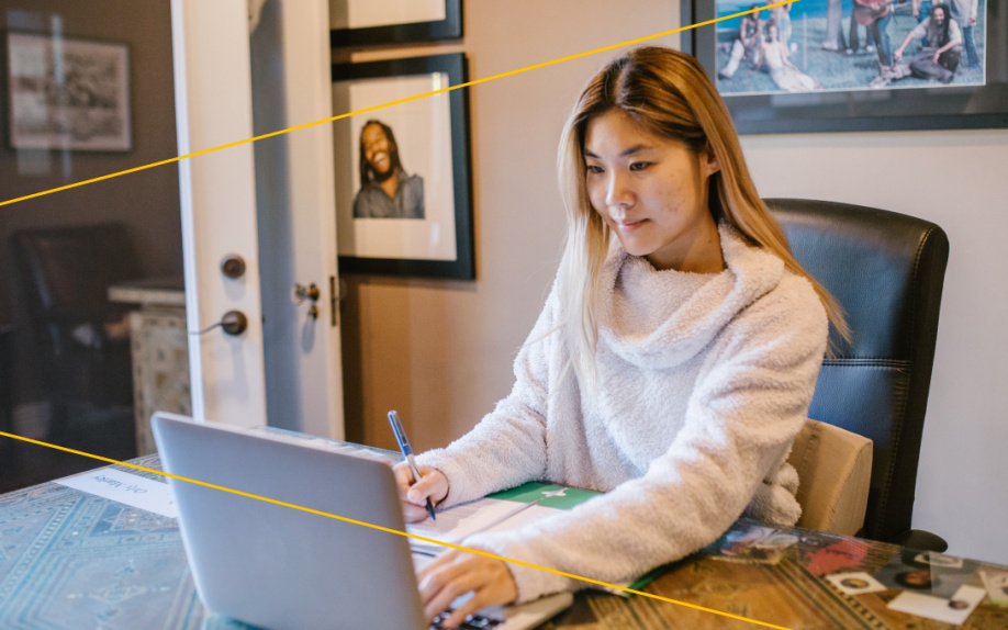 Photo of a woman, seated, wearing a white sweater and using a silver laptop computer