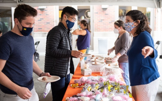 Photo of Susan Guindi (right) and students (left) at the Fall Festival 2021. They stand on either side of a table with individually packaged food and snacks.