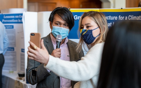 Photo of two students presenting their Gramlich poster live on Instagram. Student on the left holding microphone, student on right holding phone.