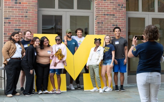Photo of a group of students and alumni in front of a large maize-colored Block M
