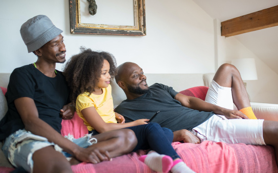Photo of a young family on the couch, smiling, watching something off to the side