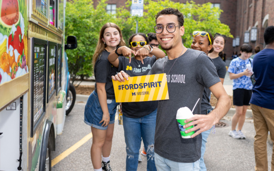 PPIA fellows smiling, holding "#Fordspirit" sign, near food truck