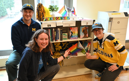 Photo of Michael Fuller, Anna Pomper, and Dominique Baeta posing in front of bookshelf