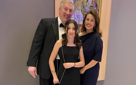 Three people in formal attire posing for a photo, with a colorful abstract artwork in the background.