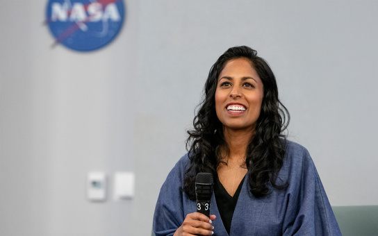 Person holding a microphone, smiling during a presentation at a NASA facility.