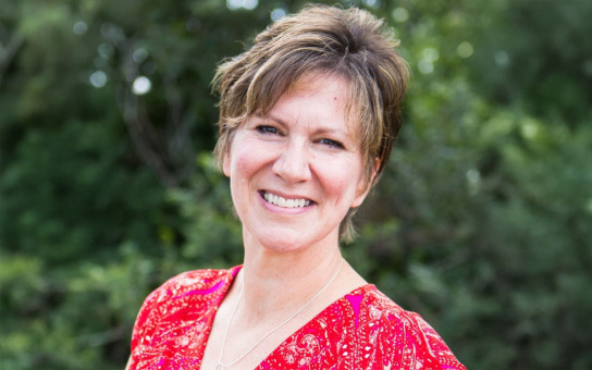 Portrait of a smiling individual in a red blouse with a natural green background.
