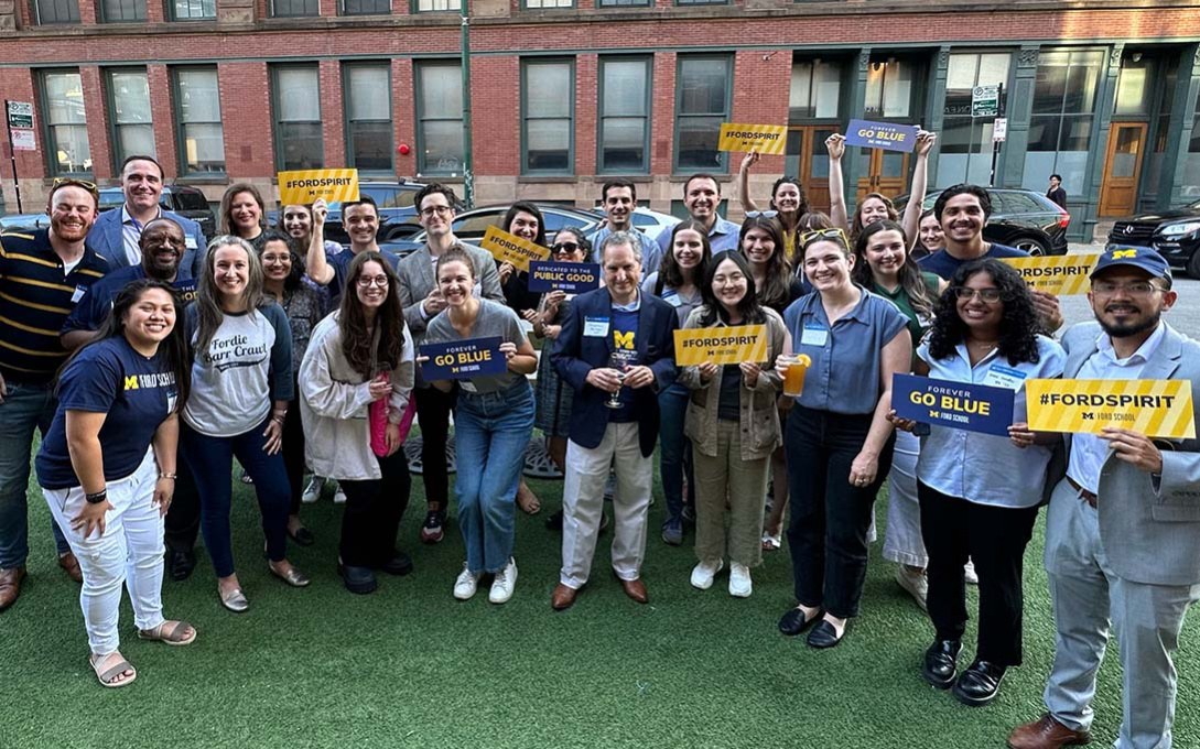 Attendees of 2023 Spirit Day in Chicago gathered outside, smiling and holding maize signs that read #FORDSPIRIT