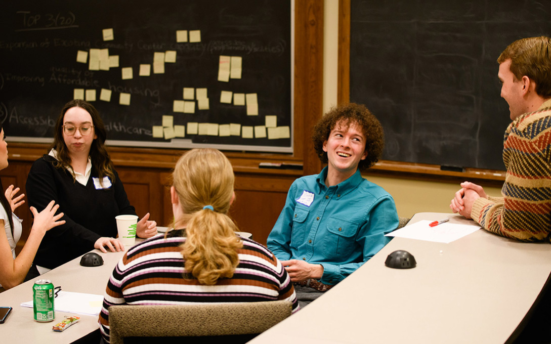 Students talking in a classroom with sticky notes on a chalkboard behind them